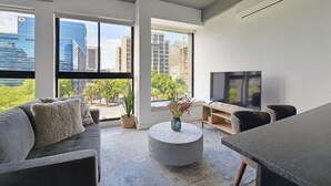 A modern living room with a sofa, coffee table, and TV, large windows with city views, and a potted plant. - Modern City Escape with Rooftop Pool Views (Cape Town)