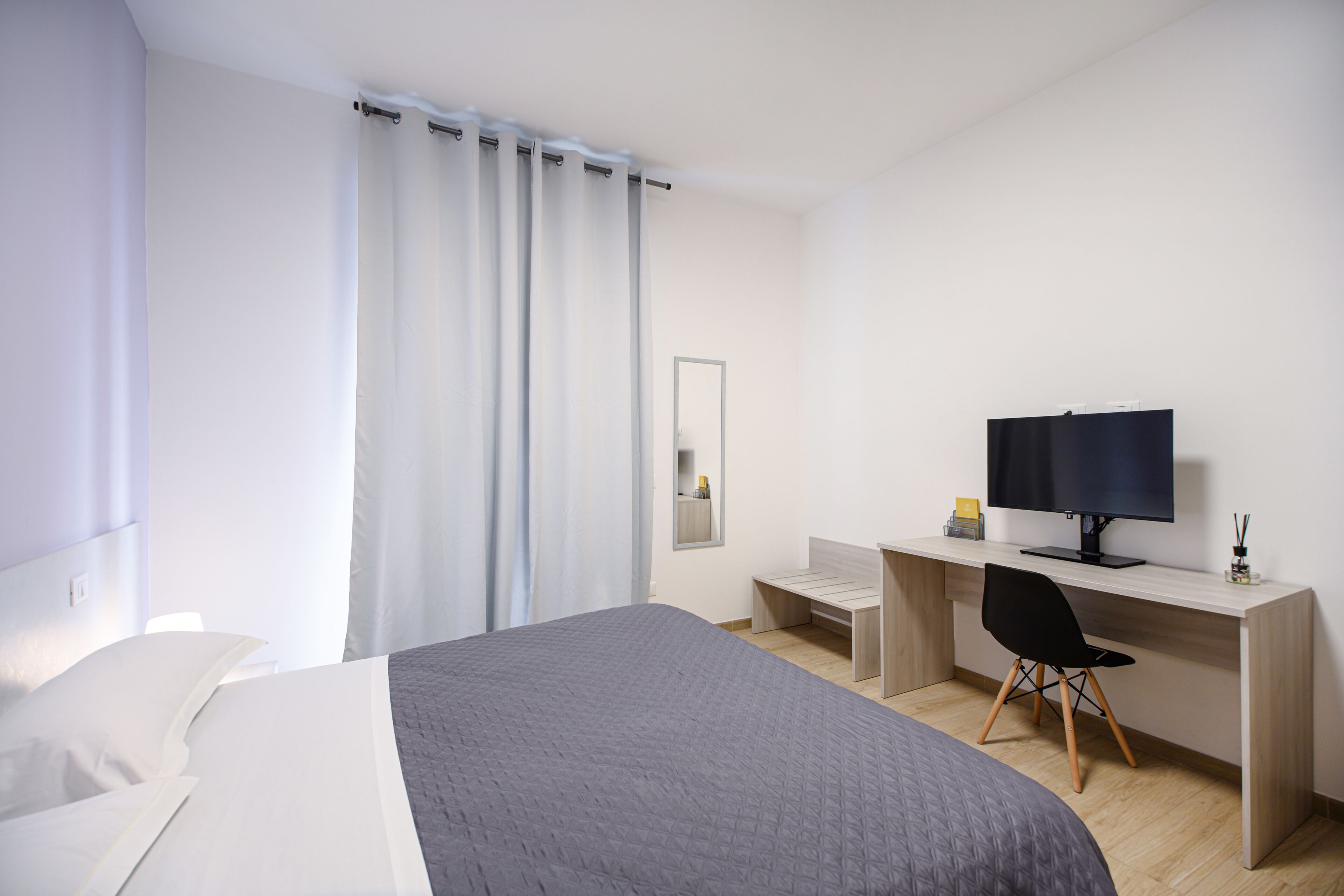 Ett modernt hotellrum med en stor säng, ett skrivbord med en dator och en stol.