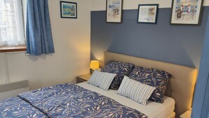 A bedroom with a bed, a nightstand, a lamp, and framed pictures on the wall.