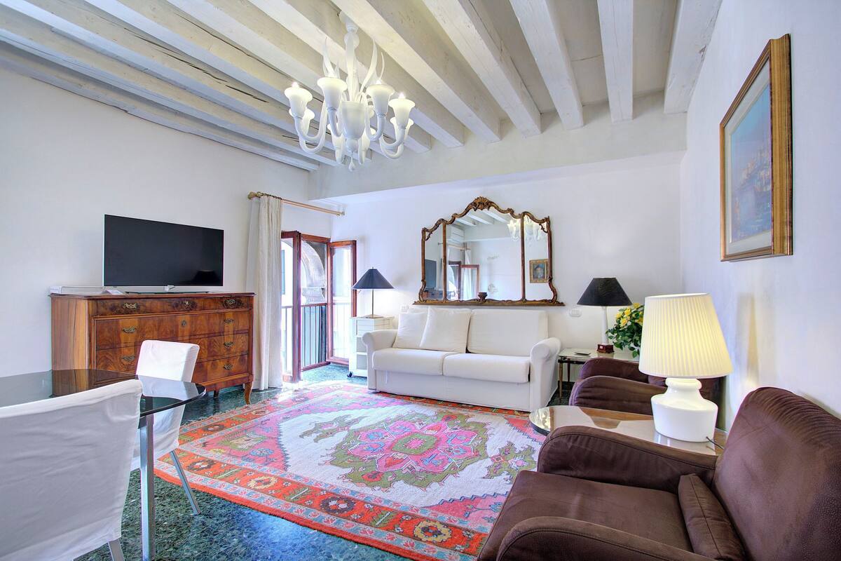 A living room with a television, sofa, armchair, and a patterned rug.