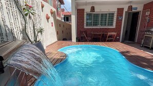 A swimming pool with a waterfall feature, surrounded by a patio area with a brick wall and a door labeled "m Vindo". - Casa com Piscina a 40 metros do Mar by La Playa (Ipojuca)