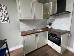 Una cocina compacta con armarios blancos, encimera de madera, pileta de acero inoxidable y horno empotrado.