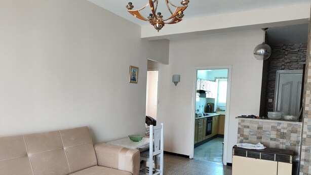 A living room with a beige sofa, a patterned rug, and a kitchen visible through an open doorway. - Appartement Alger vue sur Mer (Hussein Dey)