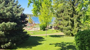 En park med et legeplads, en blå himmel og et vandareal i baggrunden.