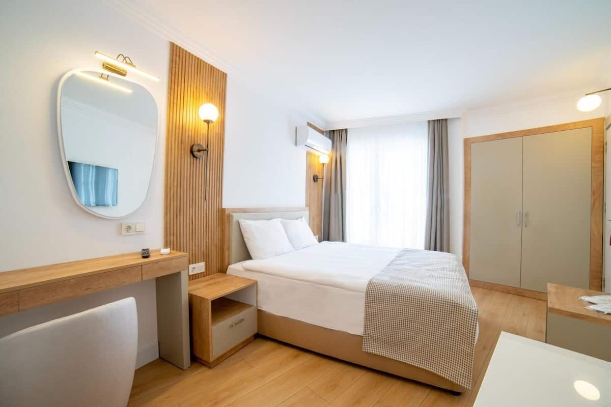 Una habitación de hotel moderna con cama, mesita de noche, espejo y armario.