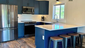 Une cuisine moderne avec des meubles bleu foncé, des appareils en acier inoxydable, un grand îlot central doté de tabourets et un plafond en bois.