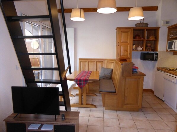 A compact kitchen with wooden cabinets, a dining area with a bench, and a staircase.
