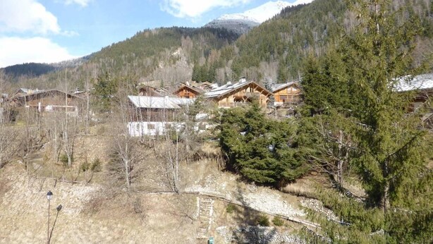 Ein Bergdorf mit Holzhäusern, wolkenlosem Himmel und schneebedeckten Berggipfeln im Hintergrund.