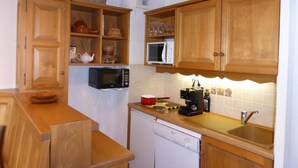 Eine kleine Küche mit Holzschränken, einer Mikrowelle, einem Geschirrspüler und einem Spülbecken.
