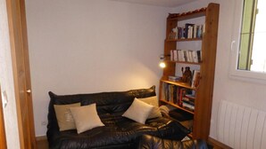 Ein gemütliches Wohnzimmer mit einer schwarzen Ledersofa, einem hölzernen Bücherregal und einem Fenster mit Jalousien.