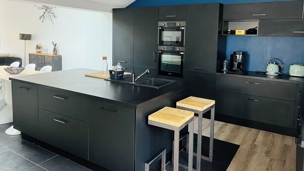 Cozinha moderna com armários escuros, ilha central e banquetas.