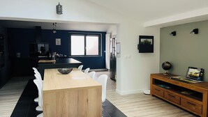 Uma cozinha moderna com uma ilha central, uma sala de jantar com mesa de madeira e cadeiras brancas, e uma sala de estar com armário de madeira e um globo.