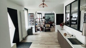 Uma sala de estar moderna com piso de madeira, estante de livros, área de jantar e uma janela grande.