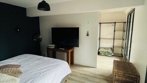 Quarto com cama, televisão, escrivaninha e escada para uma varanda.