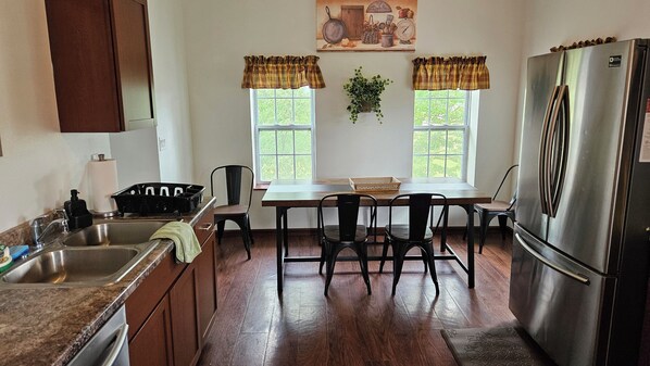 A kitchen with a stainless steel refrigerator, wooden cabinets, a sink, and a dining table with chairs.