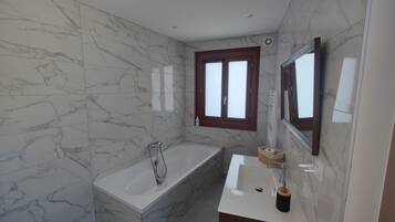 A modern bathroom with marble walls, a bathtub, a sink, and a window.