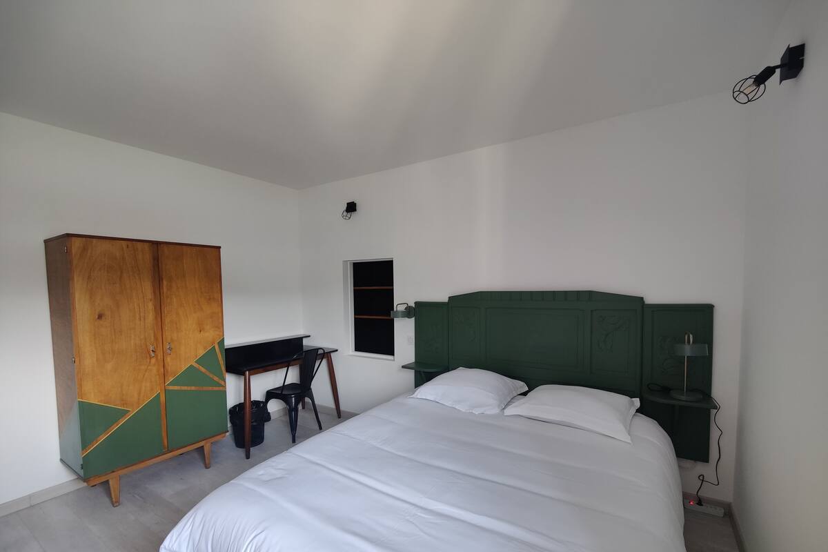 Quarto com cama, guarda-roupa de madeira, escrivaninha e cabeceira verde.