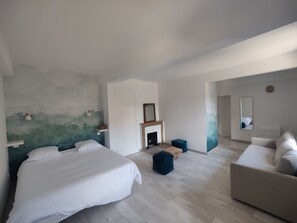 A modern bedroom with a large bed, a sofa, a fireplace, and a mirror.