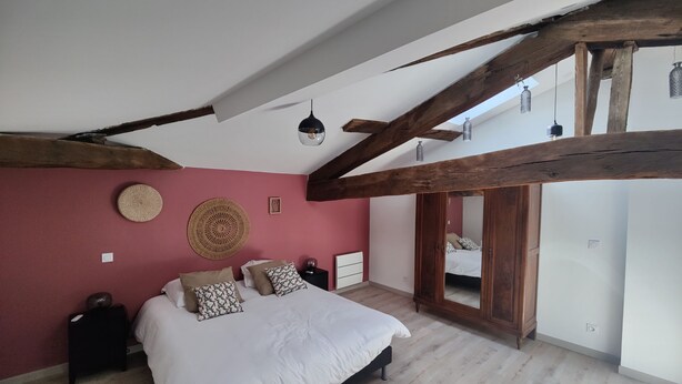 Une chambre avec un plafond en pente, un lit avec une literie blanche, une décoration murale ronde en fibres tressées et une armoire en bois.