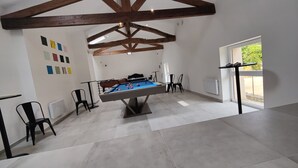 Une pièce spacieuse équipée d’une table de billard, de chaises noires et d’une fenêtre donnant sur un paysage verdoyant.