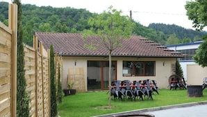 Un bâtiment avec un toit recouvert de tuiles, un petit arbre dans la cour et des sièges extérieurs avec des chaises.