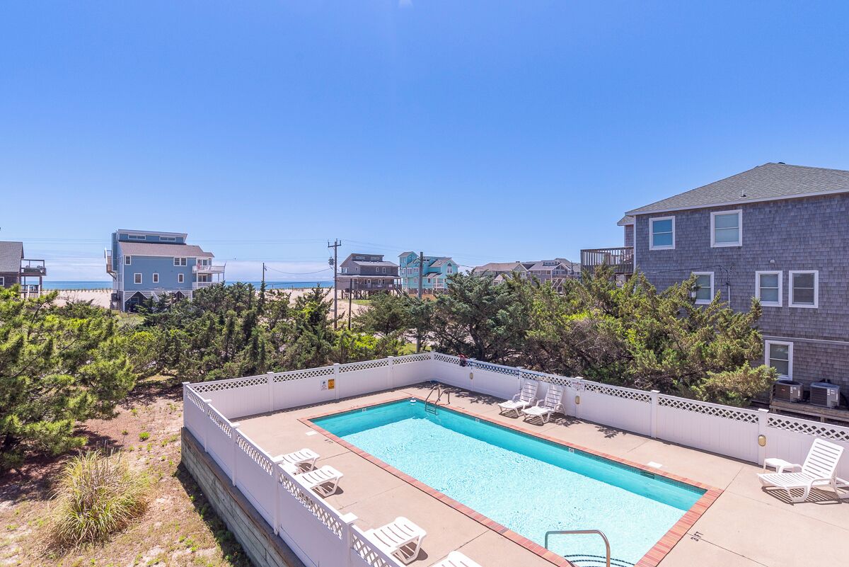 A swimming pool with lounge chairs, surrounded by a wooden deck and a white fence.