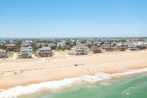 A coastal residential area with houses along the beach, a sandy beach, and ocean waves.