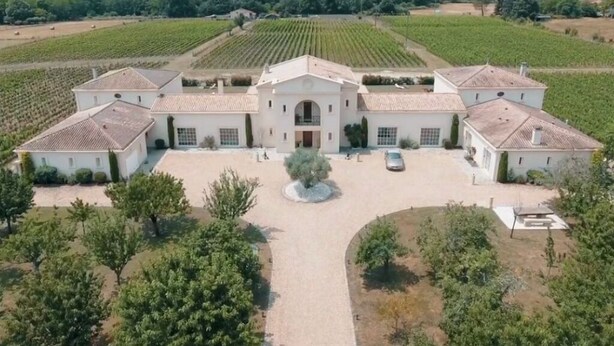 Un grand bâtiment blanc à la façade symétrique, entouré de vignes, ce qui laisse supposer qu’il pourrait s’agir d’un domaine viticole ou d’un château.