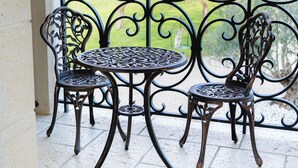 Un balcon doté d’une balustrade en fer forgé, de deux chaises et d’une petite table ronde.