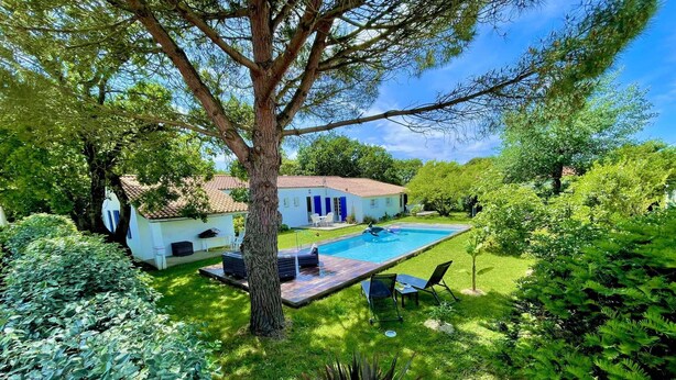 Una casa con piscina, rodeada de abundante vegetación y un árbol grande.