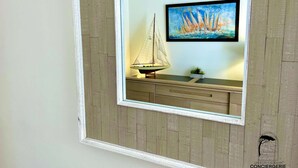 Una obra de arte enmarco con un velero y un barco en un muelle, una planta pequeña y un aplique de pared.