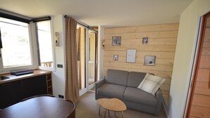 A compact living space with a sofa, a small table, a kitchen area with a sink, and a sliding glass door leading to an outdoor area. - 30m from ski lifts, 2nd floor, view ski slopes, terrace, tv, ski locker, 19m², Montalbert (La Plagne)