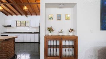 A kitchen with white cabinets, a brick counter, and a wooden cabinet with glass doors. There are three potted plants on top of the wooden cabinet.
