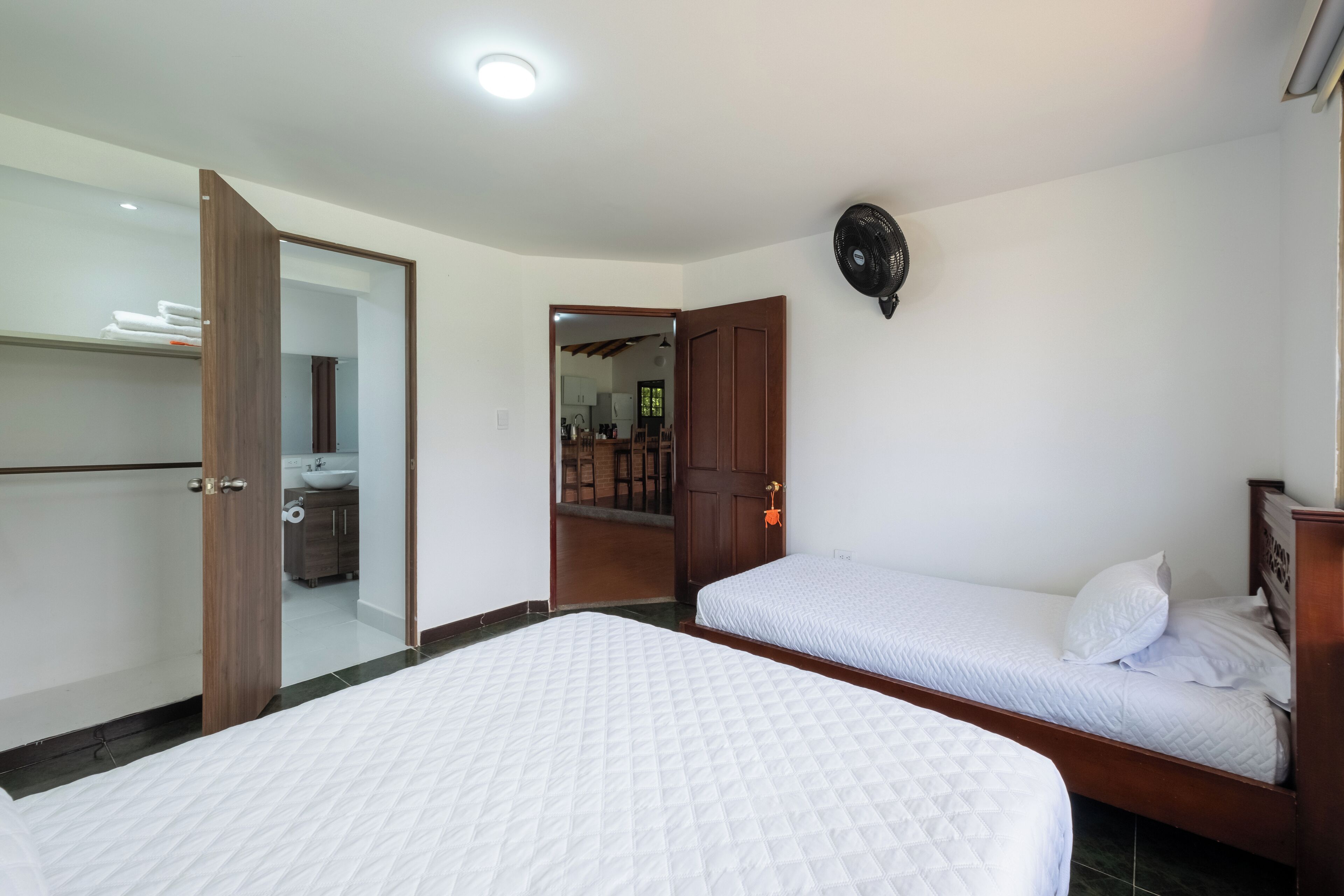 A bedroom with two beds, a wooden wardrobe, a mirror, and a ceiling fan.