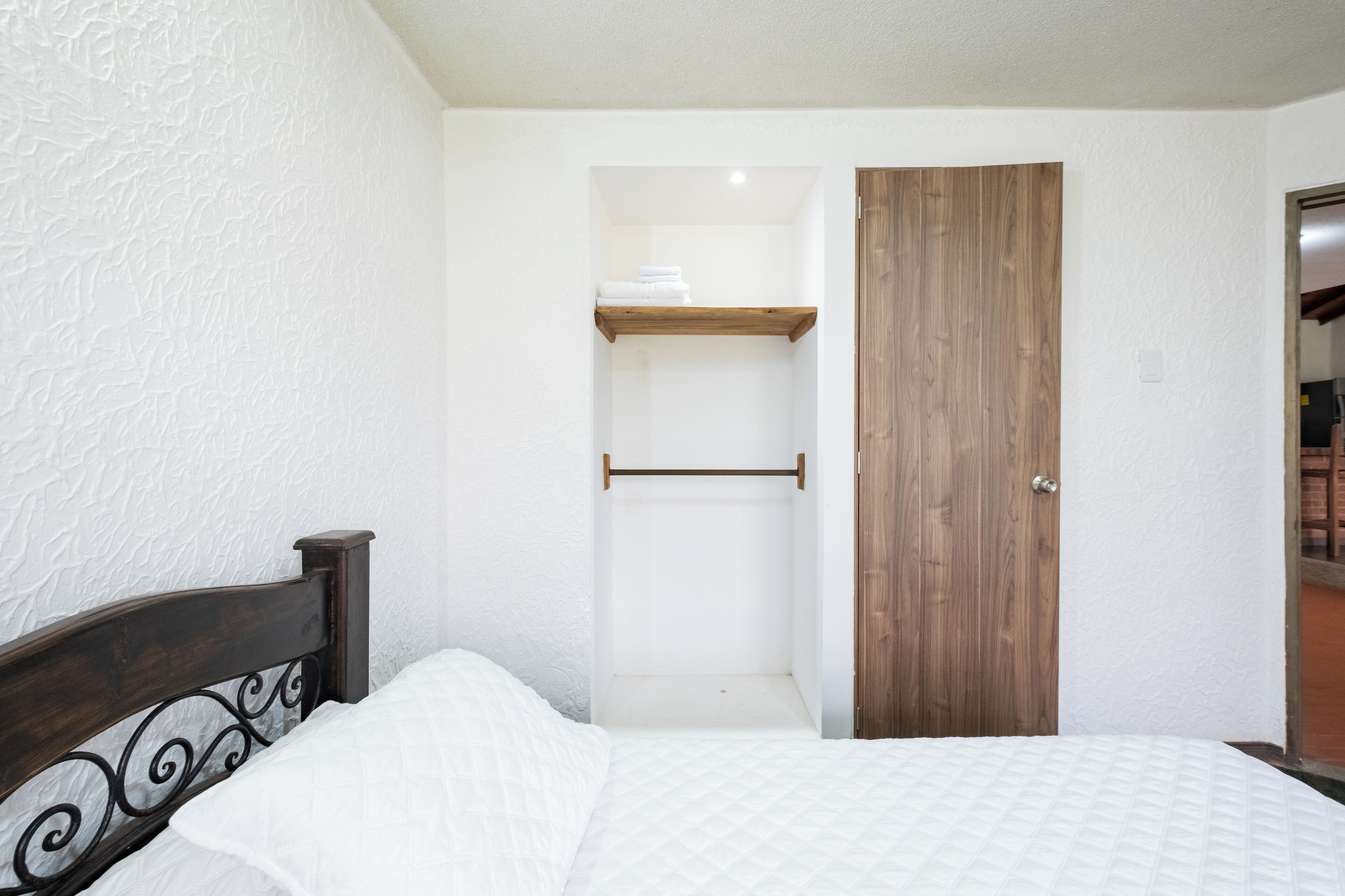 A bedroom with a wooden headboard, a bed with white bedding, a wooden door, and a white textured wall.
