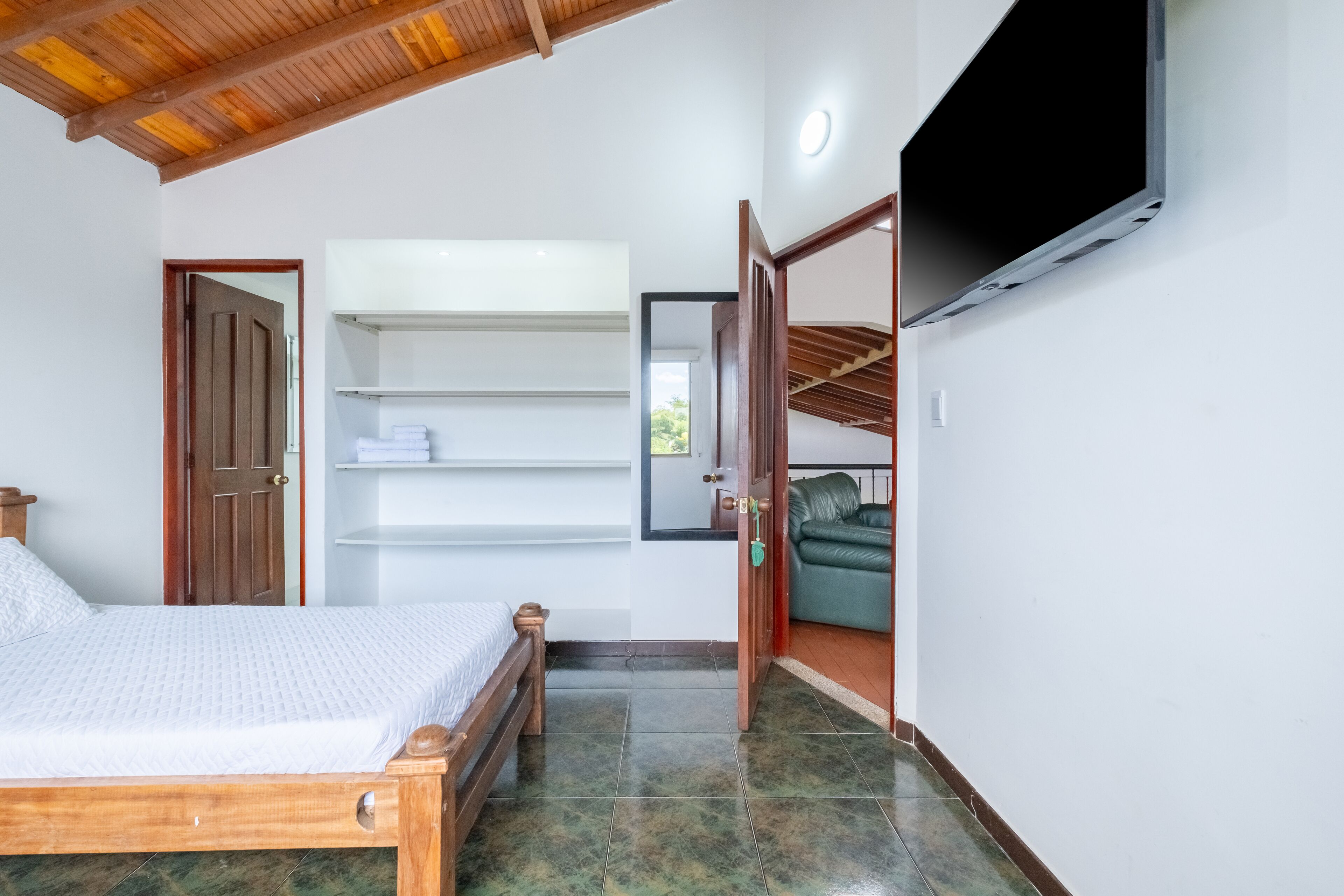 A bedroom with a wooden bed, a TV mounted on the wall, and a green chair in the corner.