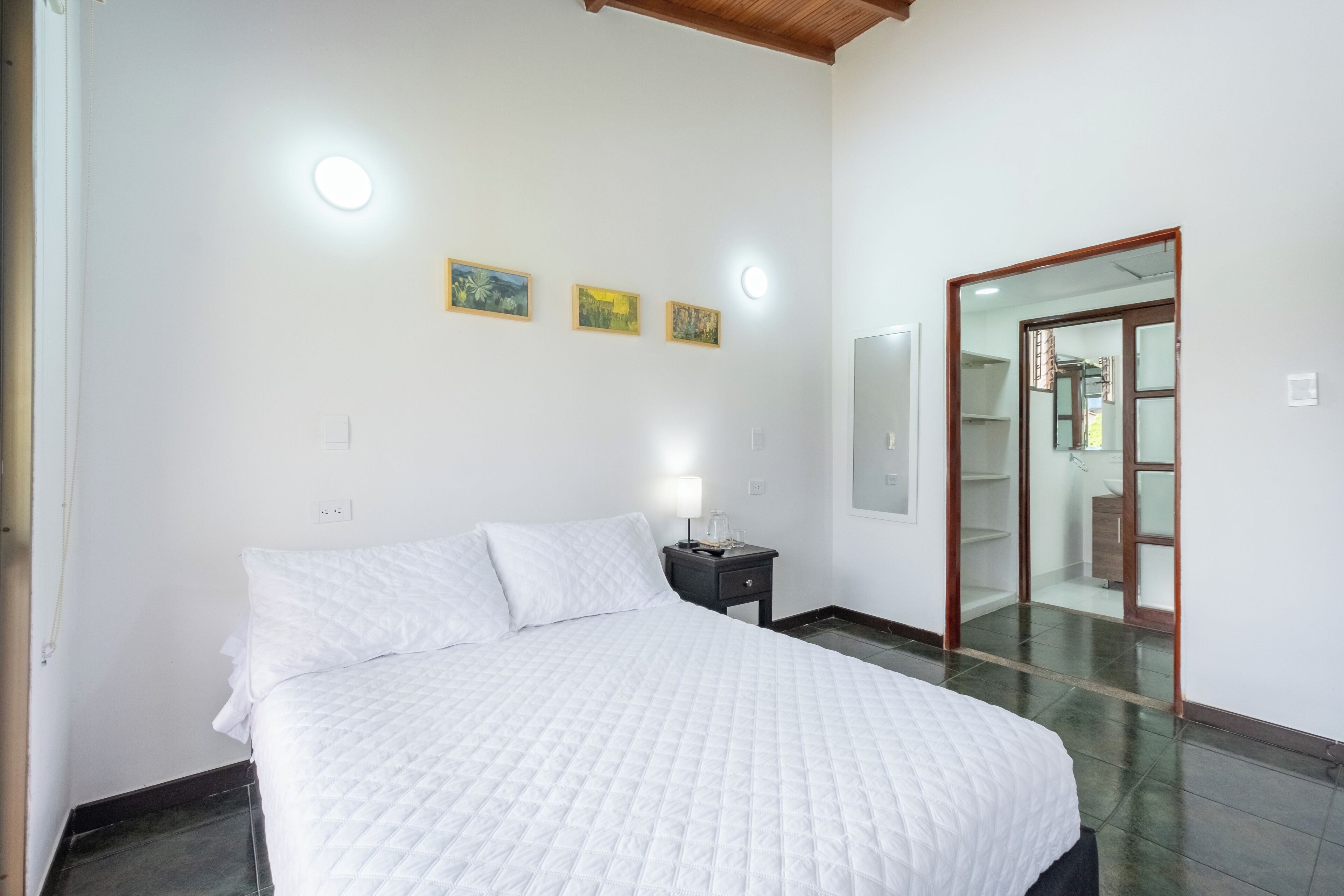 A bedroom with a large bed, a bedside table with a lamp, and three framed pictures on the wall.