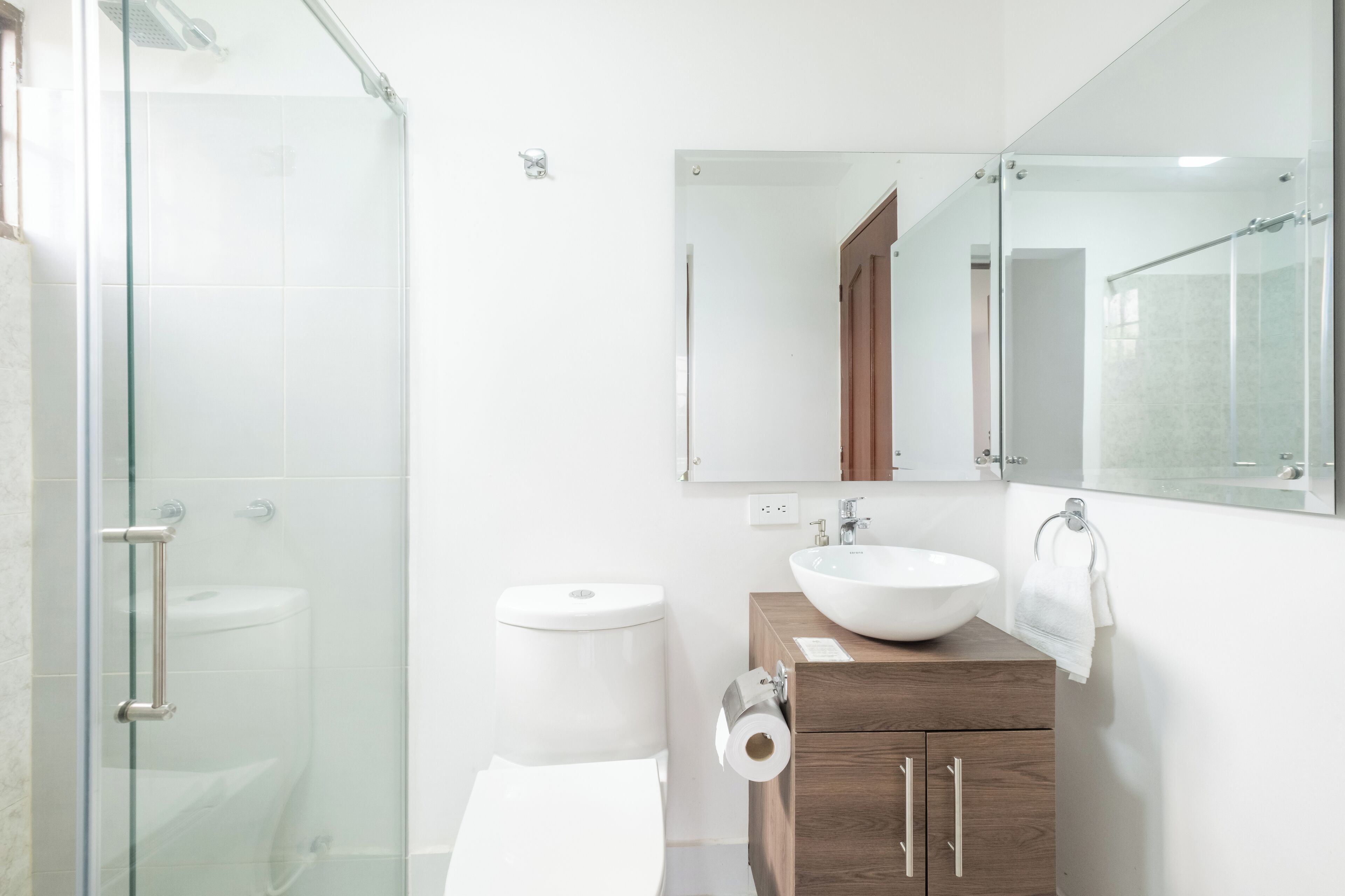A modern bathroom with a glass shower enclosure, a white toilet, a wooden vanity with a sink, and a large mirror.