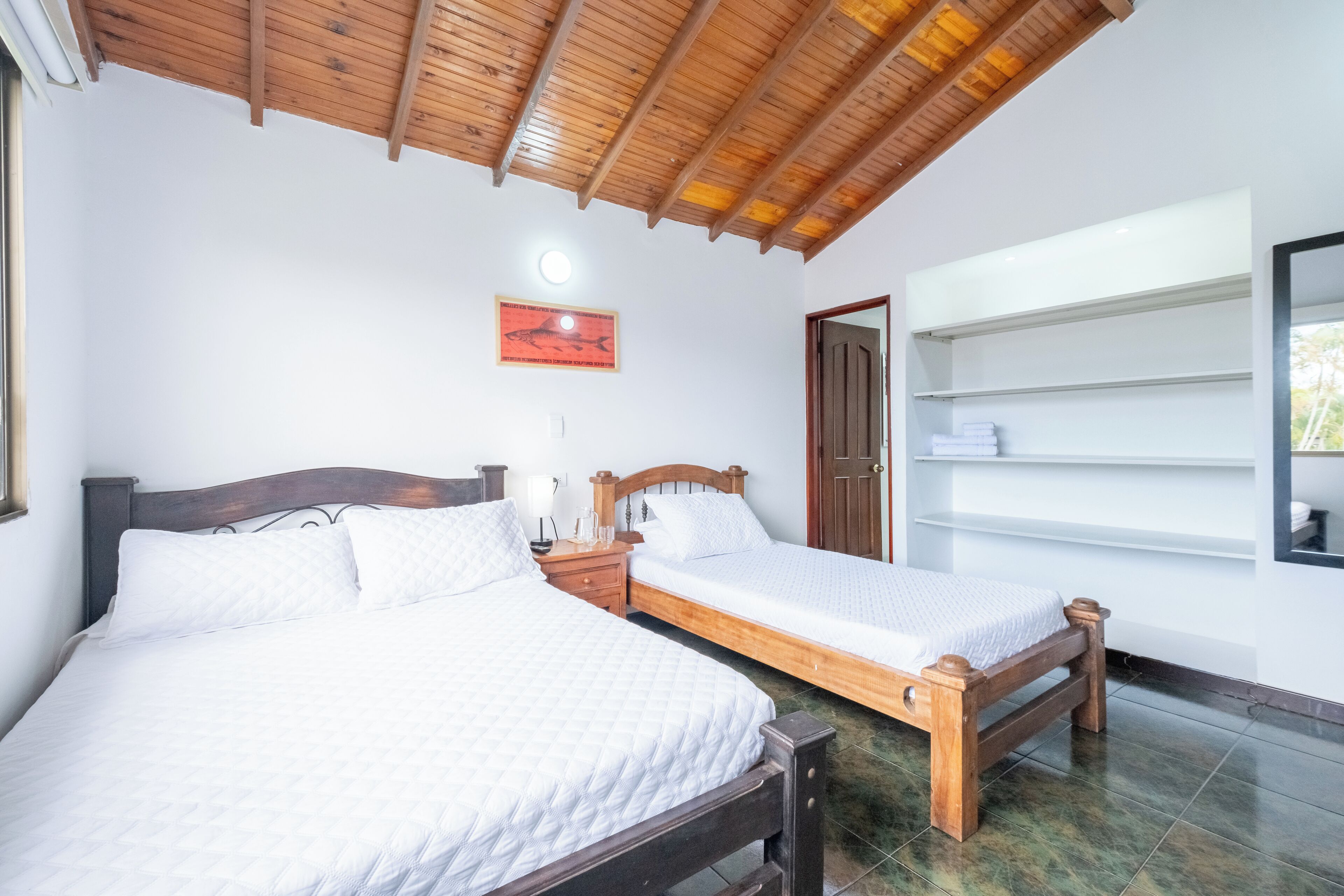 Een slaapkamer met twee houten bedden, een houten plafond, een witte muur en een lijst met een afbeelding.