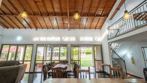 A spacious dining area with wooden tables and chairs, large windows offering views of the outdoors, and a wooden ceiling with hanging light fixtures. - Hotel Chalet La Sofia by Majuva (Armenia)