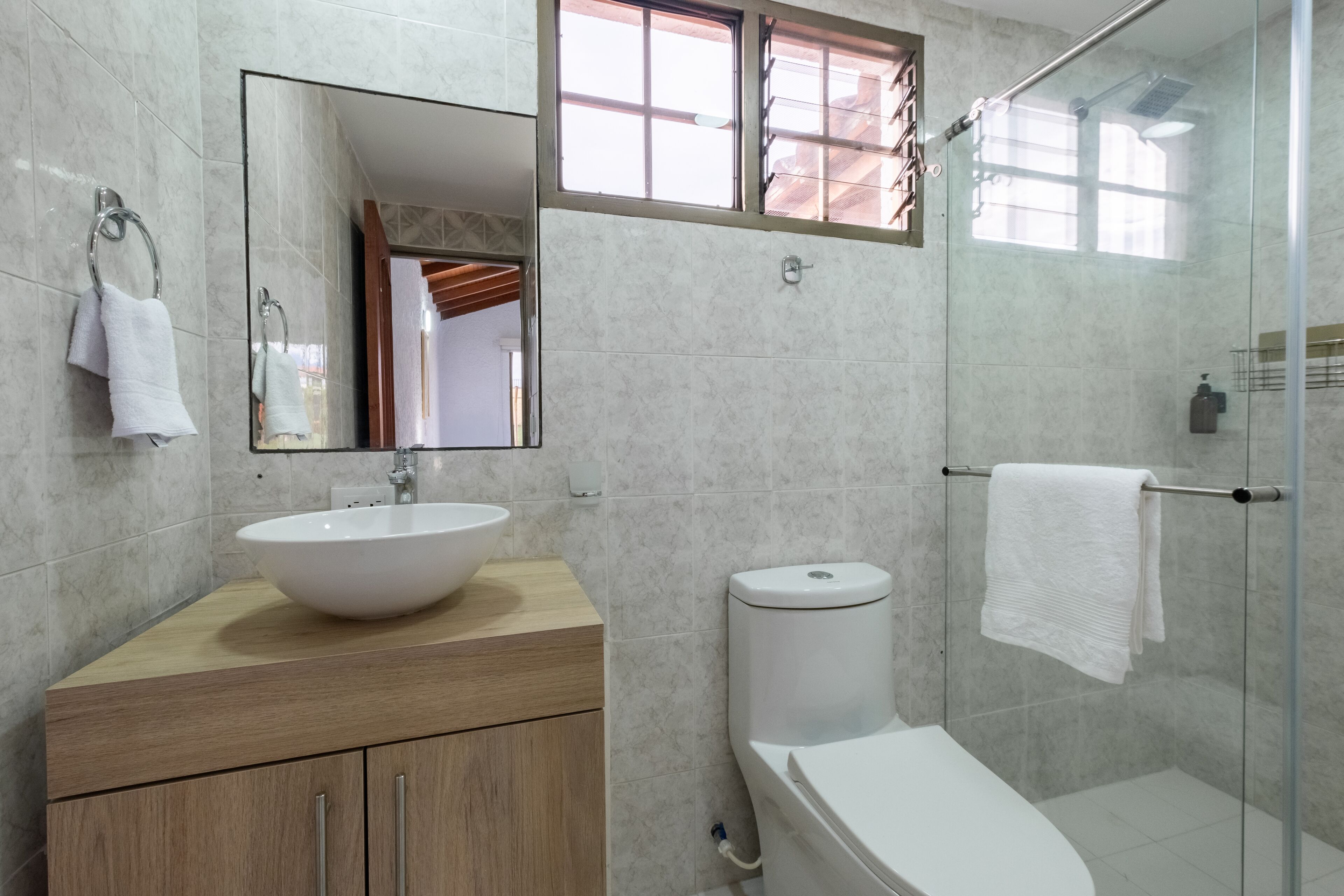 Une salle de bain moderne avec un grand miroir, un lavabo blanc, des toilettes et une douche séparée par une paroi de verre.