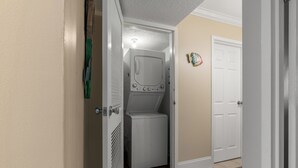 A laundry room with a front-loading washer and dryer, a door with a decorative plate, and a tiled floor. - Crescent Sands of WH-H2 3Br OF Condo (North Myrtle Beach)