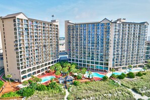 Un hotel con varias torres altas, piscina y jardines ajardinados con palmeras.