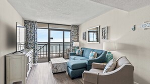 Un salon moderne avec un canapé, une table basse et un meuble. Une grande fenêtre offre une vue sur le ciel.