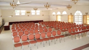 A large hall with rows of red chairs, chandeliers, and arched windows. - Koel Tourist Resort (Kaithal)
