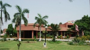 A building with a red roof and multiple windows, surrounded by palm trees and a well-maintained lawn. - Koel Tourist Resort (Kaithal)