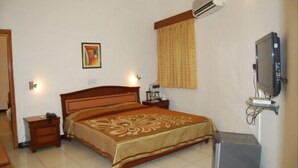 A bedroom with a bed, bedside tables, a television, an air conditioner, and a wall-mounted shelf. - Koel Tourist Resort (Kaithal)