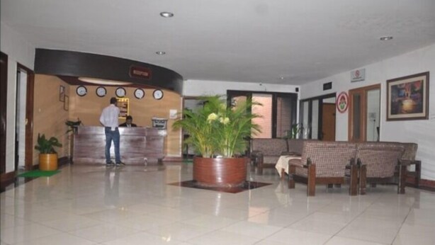 A reception area with a receptionist, a reception desk, a large potted plant, and a seating area with two chairs. - Koel Tourist Resort (Kaithal)