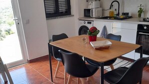 A compact kitchen with white cabinets, a microwave, and a sink. There is a dining table with chairs and a potted plant on the counter.