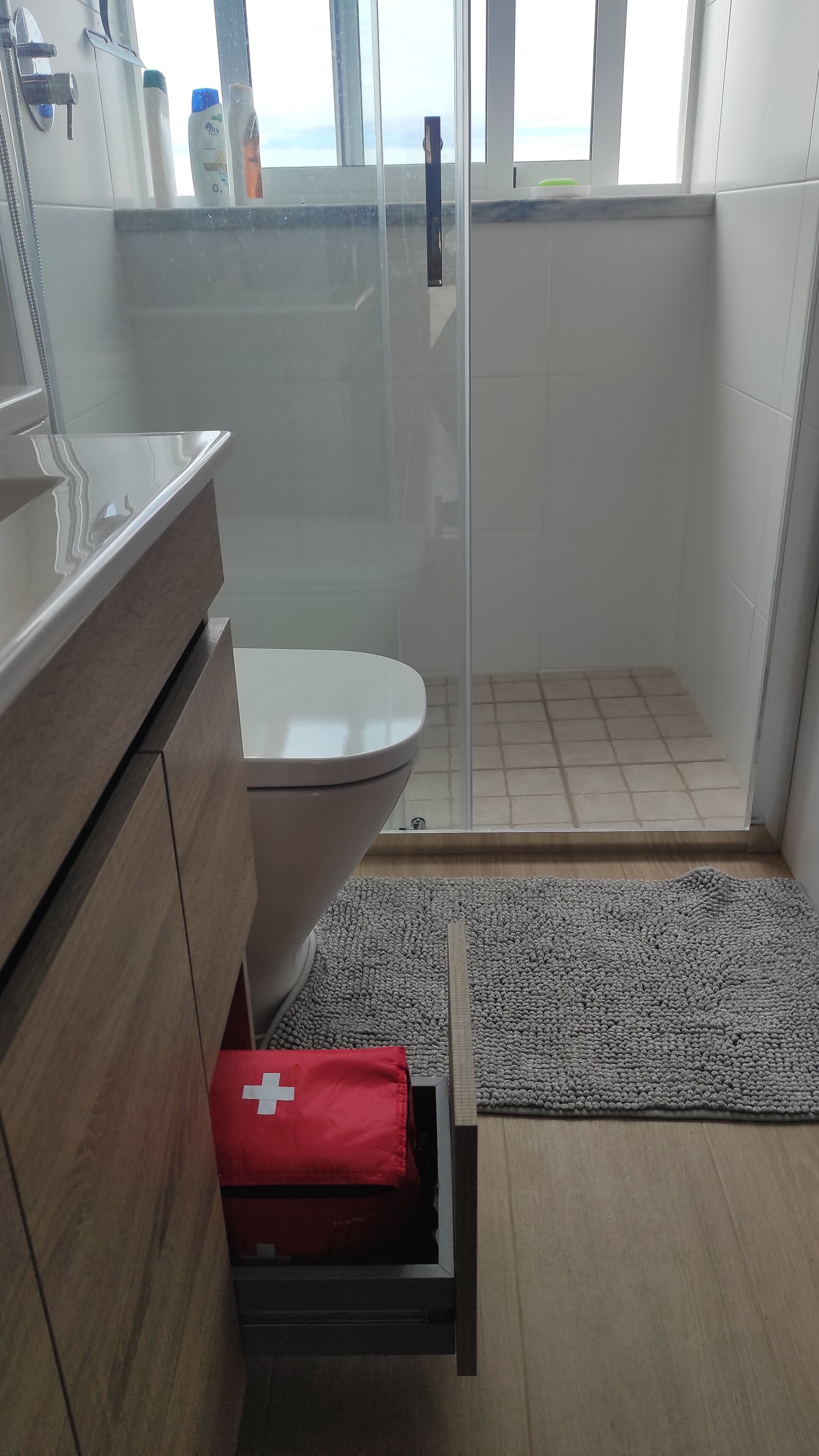 Une salle de bain moderne équipée d’une douche, de toilettes et d’une trousse de premiers secours rouge.